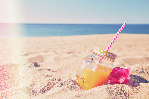 Orange juice in jar in the white sand beach. Summer concept.