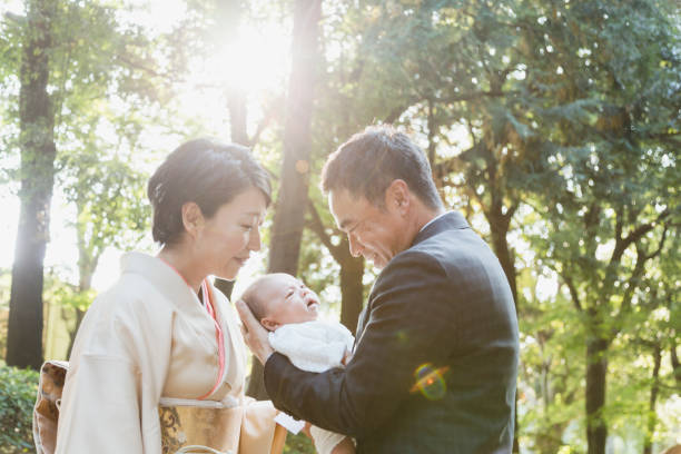 Japanese mature couple wearing formal wear carrying their new born baby Japanese father in his 50's wearing suits and mother in her 40's wearing kimono celebrating the birth of their new born baby. kimono photos stock pictures, royalty-free photos & images