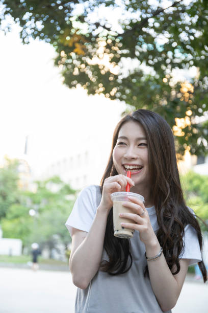 istock Woman drinking tapioca drink in park 1158436448
