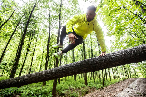 Adult Man Running in Forest in Bad Weather Adult Male Runner Jumping Across Fallen Down Tree. obstacle course stock pictures, royalty-free photos & images