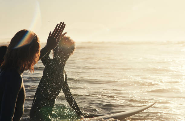 Keeping the vibe going Shot of a group of young surfers surfing together in the ocean walking in water stock pictures, royalty-free photos & images