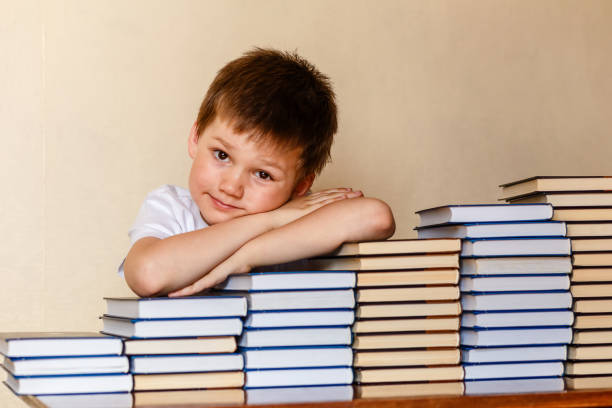 istock smiling six-year-old boy sitting at the table with his hands on books 1158450401