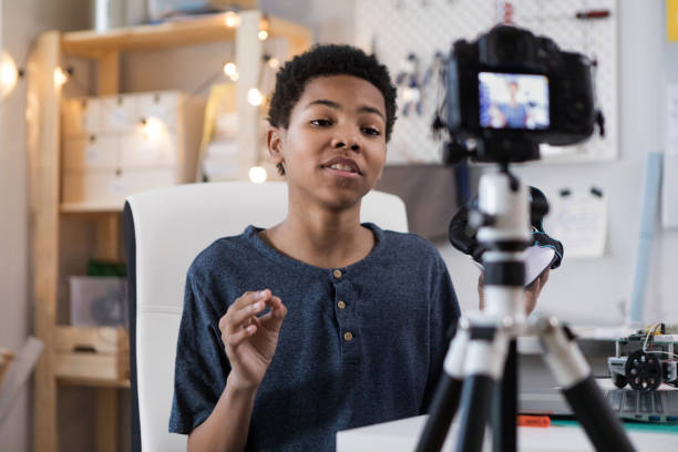 istock Preteen looks into digital camera while filming his vlog 1158450524