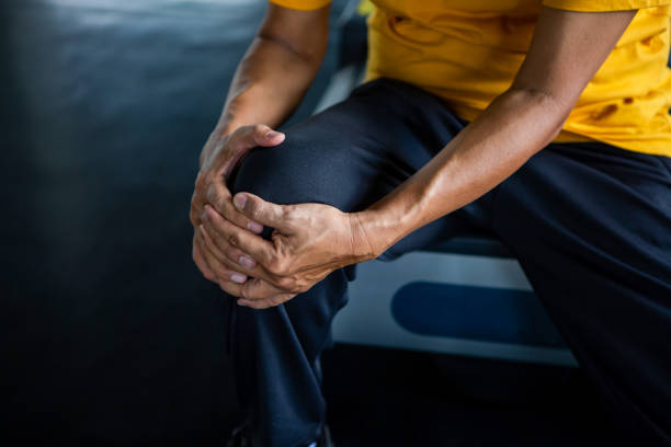 Senior asian sport man injury knee pain  sitting on treadmill in fitness gym . aged  suffering from Arthritis elder male exercising , workout, training ,healthy ,Retirement ,older, close up stock photo