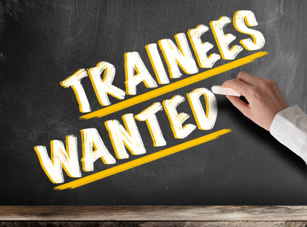istock hand holding piece of chalk against blackboard with text TRAINEES WANTED 1158453483