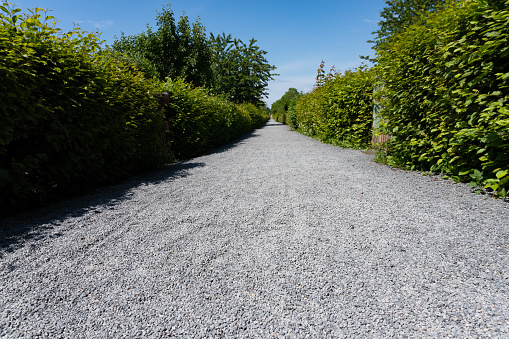 Low angle view of a long straight path with gravel in the sunlight - travel path