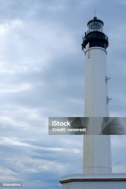 White Lighthouse Under An Overcast Sky Stock Photo - Download Image Now - Black Color, Circle, Cloud - Sky
