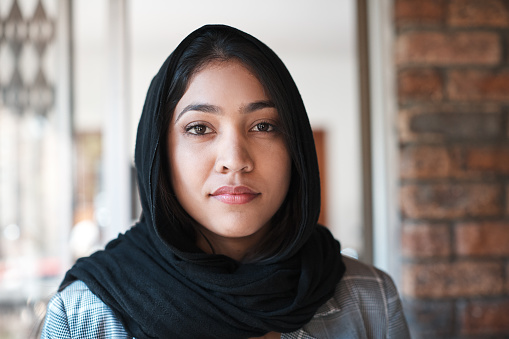 Young woman wearing a hijab standing at an entrance.