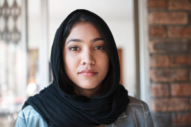 Young Muslim woman in hijab stands at the doorway of her home stock photo