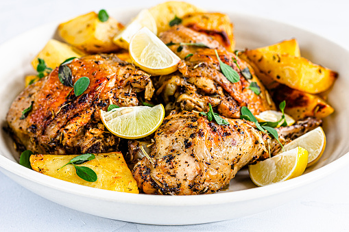 Greek Lemon Chicken with Potatoes on a Bowl Garnished with Fresh Oregano Leaves Close-Up.. Mediterranean Food Photography.