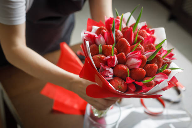 Woman in a black apron puts in a vase a beautiful original bouquet of tulips and strawberries stock photo