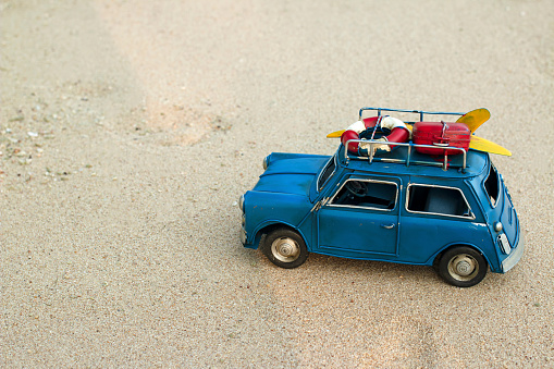 Blue toy car drive on the beach, sand, miniature metal car with lifebuoy and surfboard on the roof