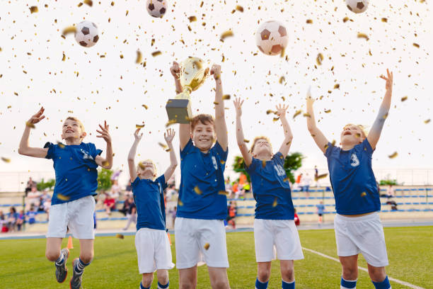 happy boys celebrando el campeonato de fútbol. el equipo ganador del fútbol juvenil y la copa de oro en la ceremonia del trofeo después del partido final del torneo. estadio de fútbol y aficionados en segundo plano - winning achievement award little boys fotografías e imágenes de stock