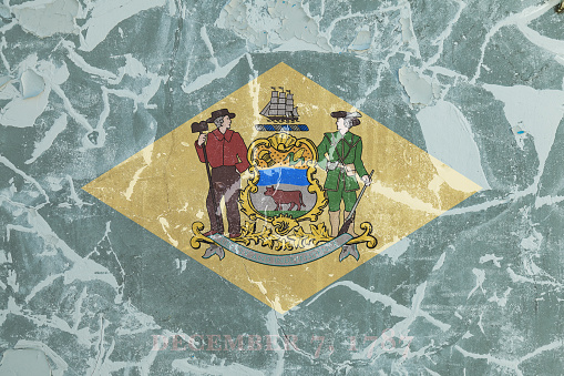 The national flag of the US state Delaware in against a gray wall with cracks and faults on the day of independence in color of green and yellow. Political and religious disputes, customs and delivery