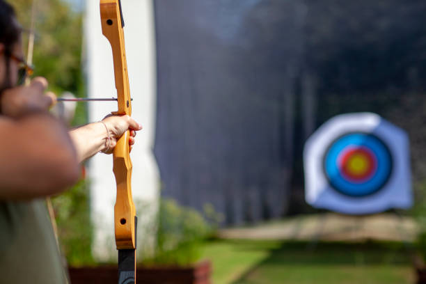 Archer holding wooden bow and aiming at unfocused target board Archer holding wooden bow and aiming at unfocused target board archery photos stock pictures, royalty-free photos & images