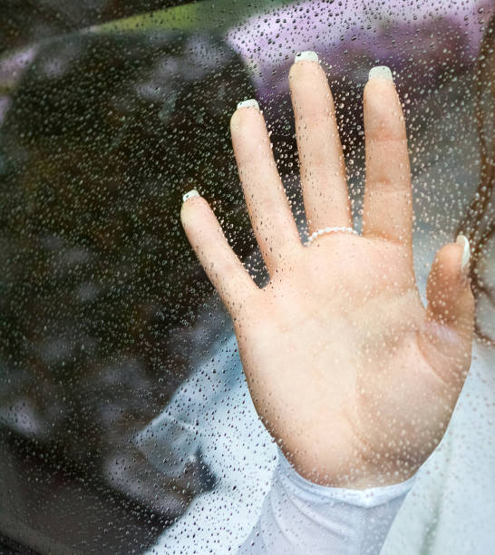 istock hand with a beautiful manicure on a window glass covered with raindrops 1158473341