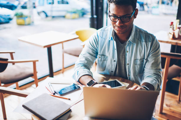 istock Cropped image of talented professional designer in eyeglasses sending email message in website on laptop computer connected to wifi.Smart male architect chatting with customer while sitting indoors 1158473645