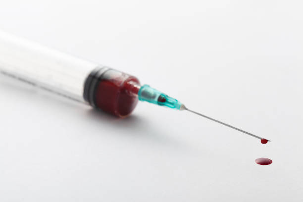 Macro view of drop of blood from syringe over white background stock photo