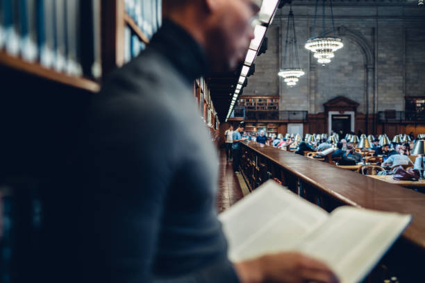 istock Selective focus on reading hall in old library of university with students spending time on education, young man holding book finding out information standing near shelves on blurred foreground 1158475884
