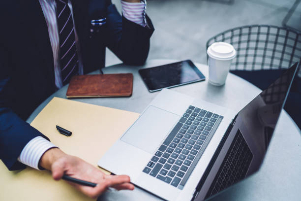 istock Cropped image of proud CEO in suit working on project sitting with laptop computer at table, close up view businessman making researches gesturing while angry about software failure on netbook 1158476111