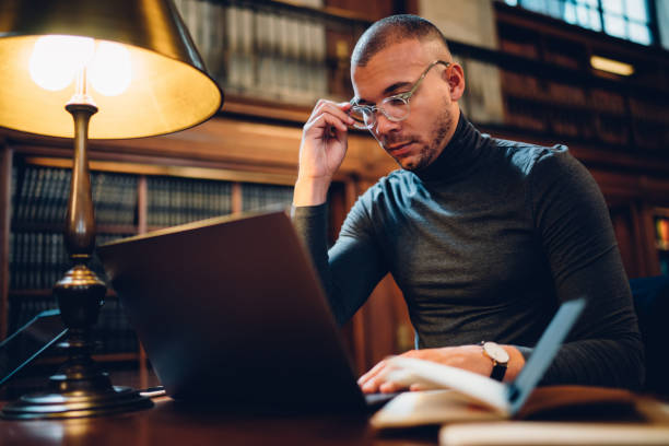 istock Adult 30 years old male student spending time in university library library for learning, intelligent man in optical spectacles searching for scientific information via modern laptop computer 1158476121