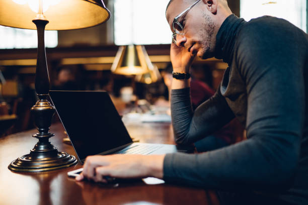 istock Thoughtful male scientist solving problems with project sitting in public library with laptop, clever journalist in eyeglasses working on article in book archive updating software on netbook 1158476140