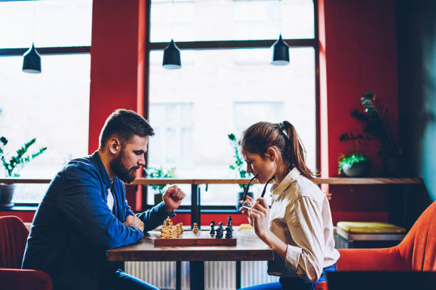istock Side view of concentrated two hipsters thinking on tactical strategy of next move on chessboard during sport competitions in chess.Young couple in love playing in favourite game in free time 1158477651