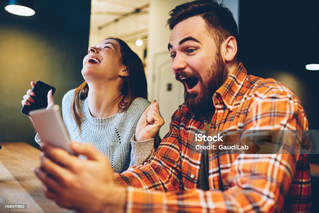 Excited male and female hipsters rejoice in winning an internet lottery made bets on website on modern smartphone.Happy couple in love celebrating victory in online competitions enjoying success Winning Stock Photo