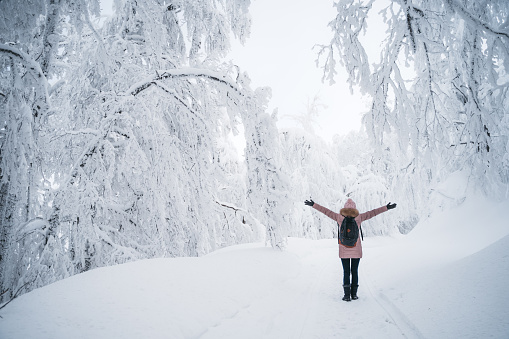 Young female in the white snowy scene. Arms outstretched. Wearing warm clothing and a backpack. Balkan mountains.