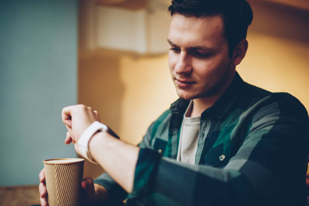 istock Young male looking at smartwatch touchscreen get notification about new message holding coffee cup, hipster guy using wearable computer apps for communication watching display settings on break 1158478799