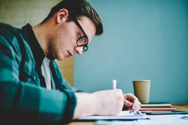 istock Close up view of smart student in spectacles writing essay for homework task concentrated on learning, serious hipster guy making accounting for startup statement idea using knowledge and creativity 1158478818