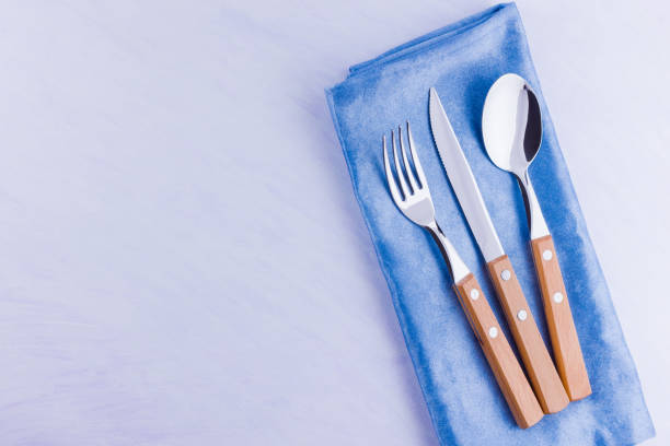 istock Cutlery set. Knife, fork, spoon on blue napkin. Table setting. Cutlery with wooden handles on a white background. Top view 1158480792