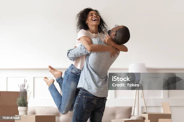 African Husband Lifting Happy Wife Celebrating Moving Day With Boxes Stock Photo - Download Image Now