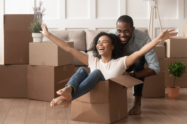 happy african young couple riding in box on moving day - moving house apartment couple box imagens e fotografias de stock