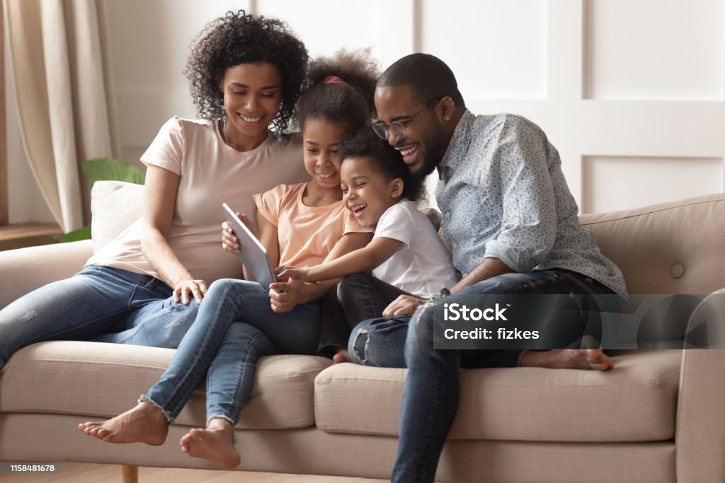 Счастливые черные родители и дети, использующие цифровой планшет на диване - Стоковые фото Семья роялти-фри