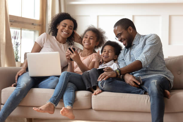les parents et les enfants africains joyeux ritnt utilisant des dispositifs sur le sofa - digital tablet women enjoyment happiness photos et images de collection