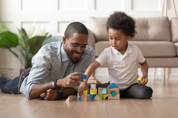 Happy african dad and child son building constructor from blocks Caring young single black father help cute kid son play on warm floor together, happy african family dad and little child boy having fun building constructor tower from colorful wooden blocks toy block photos stock pictures, royalty-free photos & images