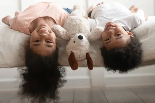 Photo of Funny little boy and girl lying upside down on bed