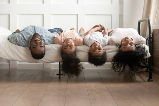glückliche afrikanische amerikanische familie bindung liegt kopfüber auf dem bett - women group of people lying down mother stock-fotos und bilder