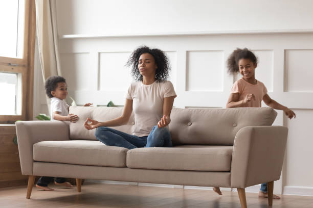 ruhige afrikanische mama macht yoga auf dem sofa entspannend mit kindern - achtsamkeit persönlichkeitseigenschaft stock-fotos und bilder