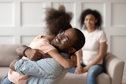 Happy african american dad embracing daughter cuddling at home, smiling black father hugging cute little kid girl bonding enjoy time together, daddy child reunion, fatherhood, child custody concept