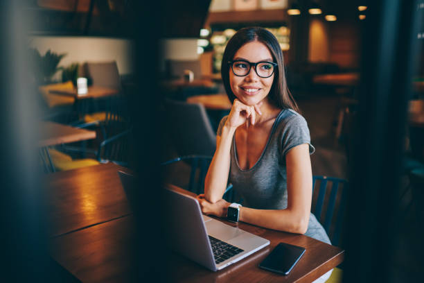 istock Attractive female freelancer in eyewear thinking about idea for project working in cafe interior, dreamy young woman in spectacles updating software on netbook for making online report for remote job 1158481885