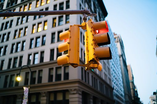 Yellow equipment for controlling transport on intersection of business district with high corporate building,red sign on traffic light hanging over crossroads in megalopolis for regulating city