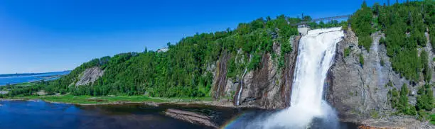 Photo of Beautiful Montmorency Falls with rainbow and blue sky. View of Canadian falls.