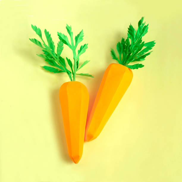 istock Two paper carrots on yellow background 1158484854