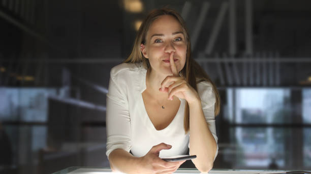 young woman librarian using her phone - silence finger on lips businesswoman one person imagens e fotografias de stock