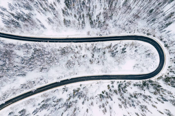 istock Curvy windy road in snow covered forest, top down aerial view. Winter landscape. 1158489630