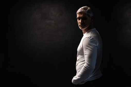 Middle-aged good looking man in white t-shirt posing in front of a black background with copy space