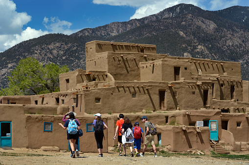 TAOS, NEW MEXICO - MAY 15, 2019: Tourists visit Taos Pueblo, an ancient Native-American pueblo near Taos, New Mexico USA. The multi-storied adobe residential complex was built between 1000 and 1450.