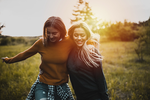 Happy two twin sisters are hugging against the background of a green blossoming apple orchard.